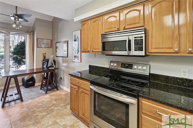 kitchen with appliances with stainless steel finishes, a ceiling fan, light tile patterned flooring, dark stone counters, and baseboards