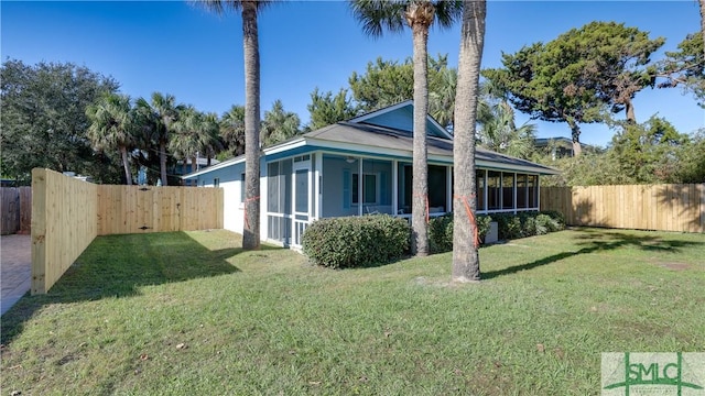 view of side of home with a yard, a fenced backyard, and a sunroom