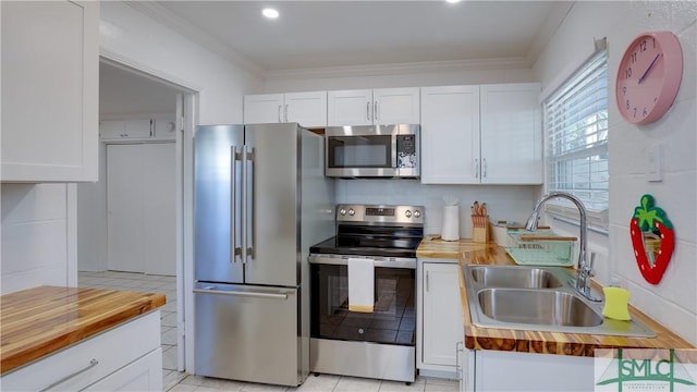 kitchen with white cabinets, wood counters, ornamental molding, stainless steel appliances, and a sink