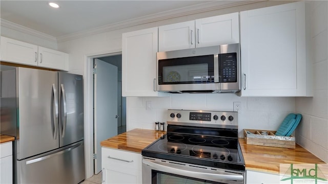 kitchen with appliances with stainless steel finishes, butcher block counters, white cabinets, and crown molding