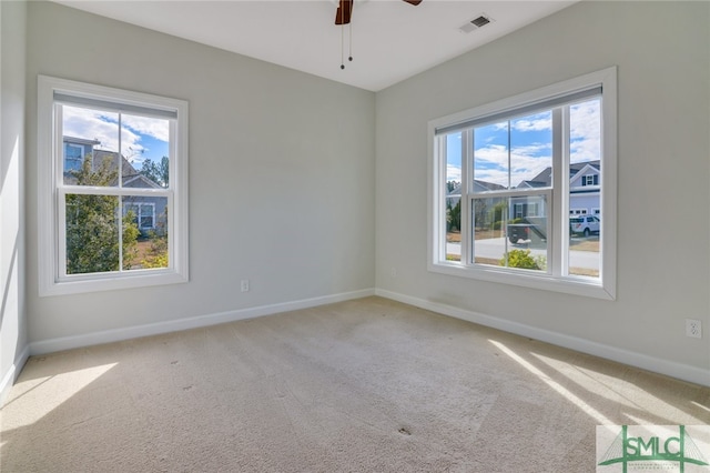 carpeted spare room featuring a wealth of natural light, visible vents, and baseboards