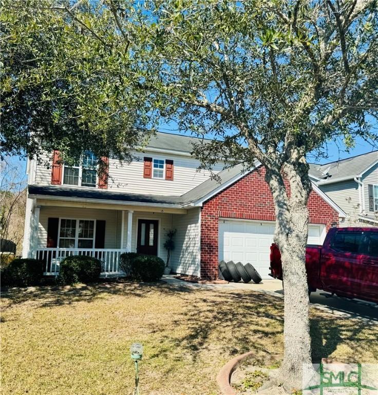 traditional-style home with a porch, a front yard, brick siding, and an attached garage