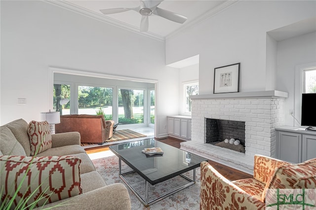 living area with a brick fireplace, ornamental molding, a towering ceiling, wood finished floors, and a ceiling fan