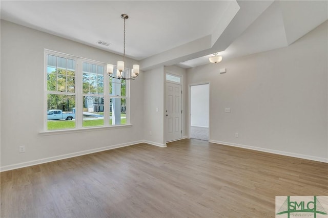 unfurnished dining area featuring a chandelier, visible vents, baseboards, and wood finished floors