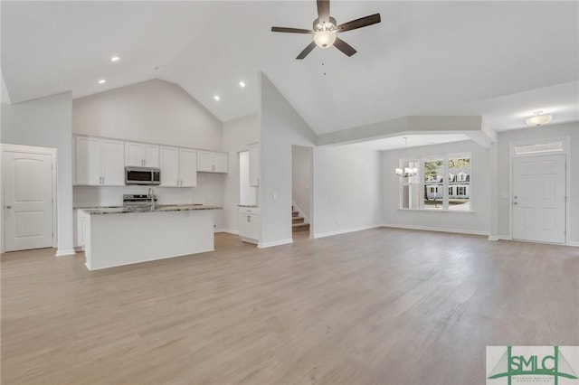 unfurnished living room featuring ceiling fan with notable chandelier, light wood-type flooring, and baseboards