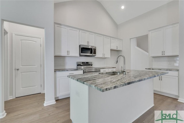 kitchen with light stone counters, stainless steel appliances, a sink, white cabinets, and light wood finished floors