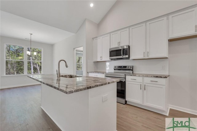 kitchen featuring stone counters, lofted ceiling, decorative backsplash, appliances with stainless steel finishes, and a sink