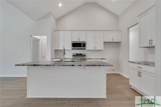 kitchen with appliances with stainless steel finishes, light wood-style floors, white cabinetry, a sink, and dark stone countertops