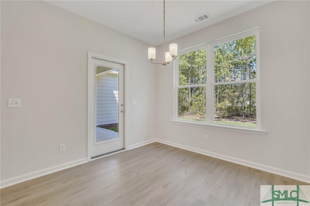 empty room featuring baseboards, wood finished floors, visible vents, and a notable chandelier