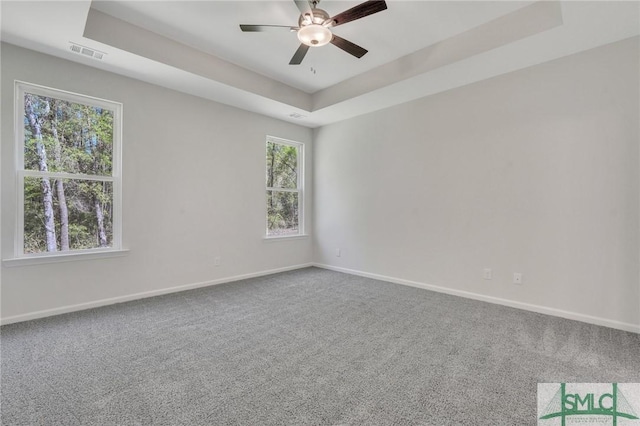 empty room featuring visible vents, baseboards, a ceiling fan, a tray ceiling, and carpet floors