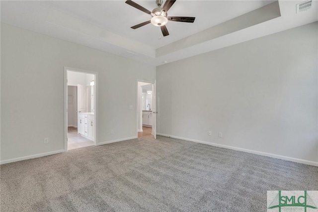 unfurnished bedroom featuring light colored carpet, visible vents, baseboards, a raised ceiling, and ensuite bath