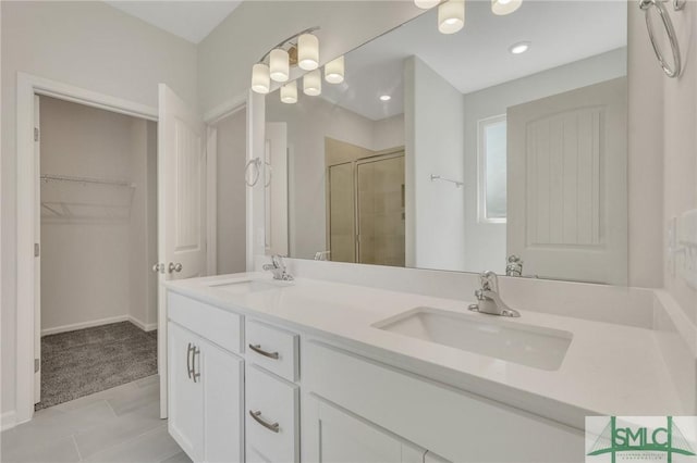 full bath featuring double vanity, a stall shower, a walk in closet, and a sink