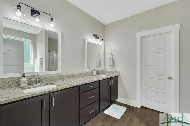 full bathroom with double vanity, a sink, baseboards, and wood finished floors