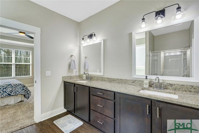 ensuite bathroom featuring wood finished floors, a sink, baseboards, double vanity, and a stall shower