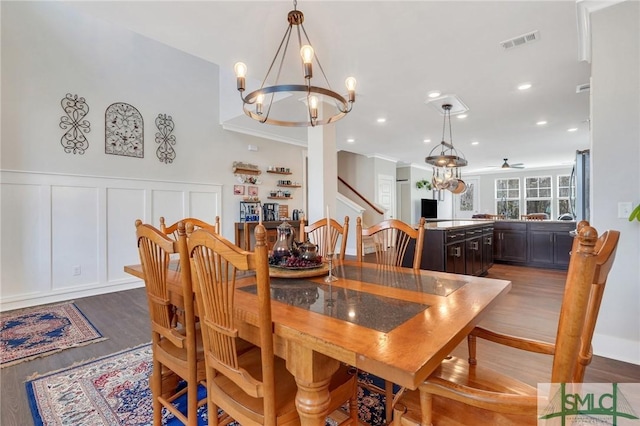 dining area featuring a notable chandelier, a decorative wall, wood finished floors, visible vents, and wainscoting