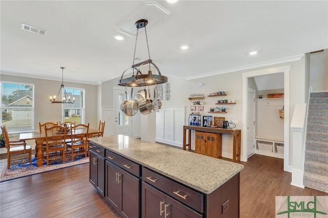 kitchen with dark wood-type flooring, visible vents, ornamental molding, light stone countertops, and decorative light fixtures