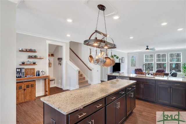 kitchen with dark wood-type flooring, a center island, light stone countertops, a sink, and recessed lighting