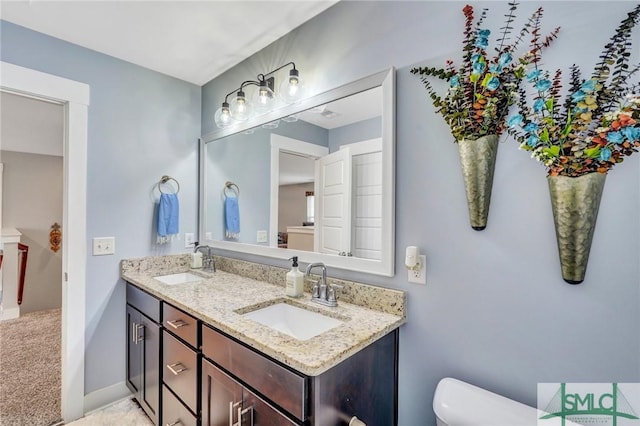 bathroom with double vanity, a sink, toilet, and baseboards