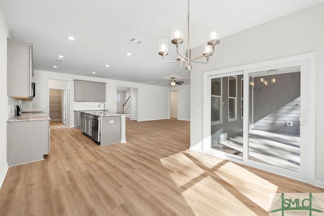 kitchen with light wood finished floors, light stone countertops, gray cabinets, a sink, and ceiling fan with notable chandelier