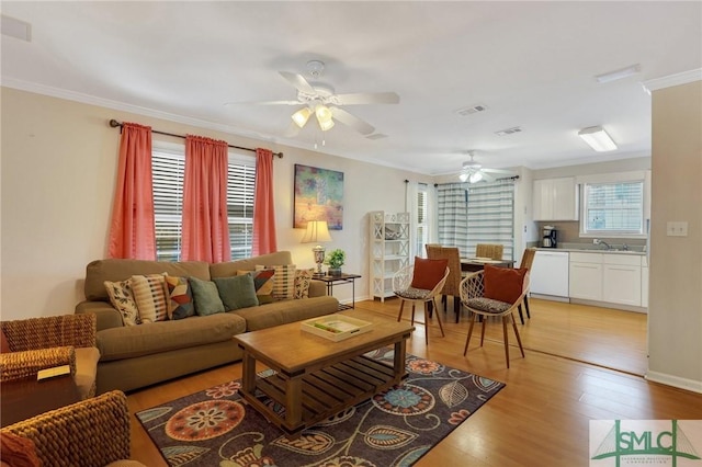 living room with crown molding, ceiling fan, plenty of natural light, and light wood-style floors