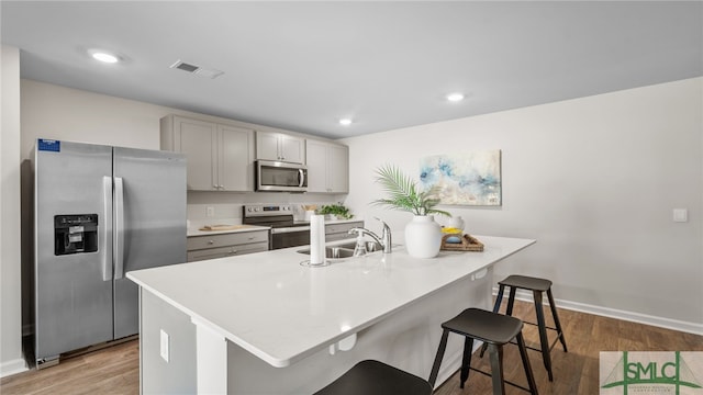 kitchen featuring gray cabinetry, wood finished floors, a sink, visible vents, and appliances with stainless steel finishes