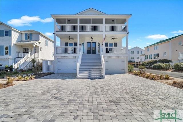 coastal inspired home with decorative driveway, a porch, stairway, a ceiling fan, and a garage