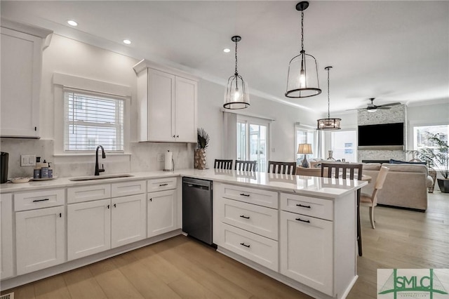 kitchen featuring light wood-style flooring, a peninsula, a sink, dishwasher, and tasteful backsplash