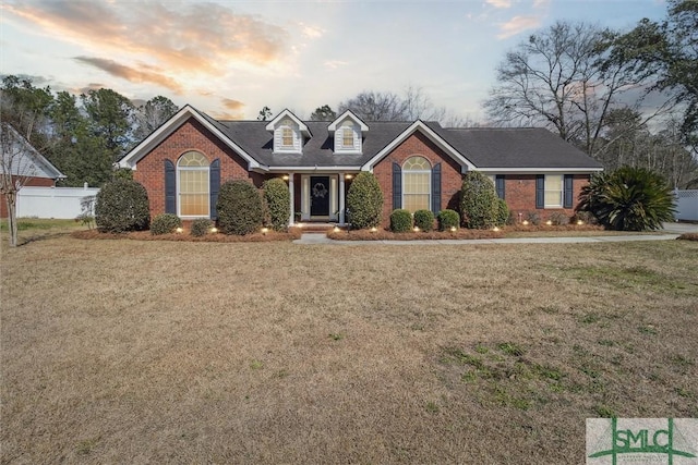 cape cod home featuring brick siding, a lawn, and fence