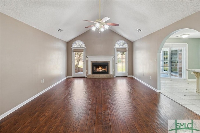 unfurnished living room with a brick fireplace, wood finished floors, visible vents, and a healthy amount of sunlight