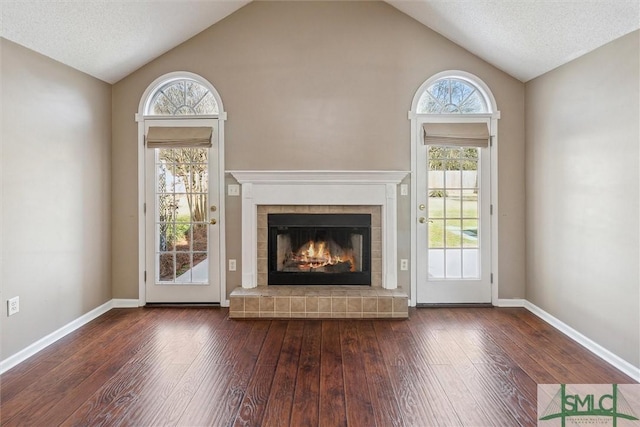 unfurnished living room featuring dark wood-style floors, a tiled fireplace, lofted ceiling, and baseboards