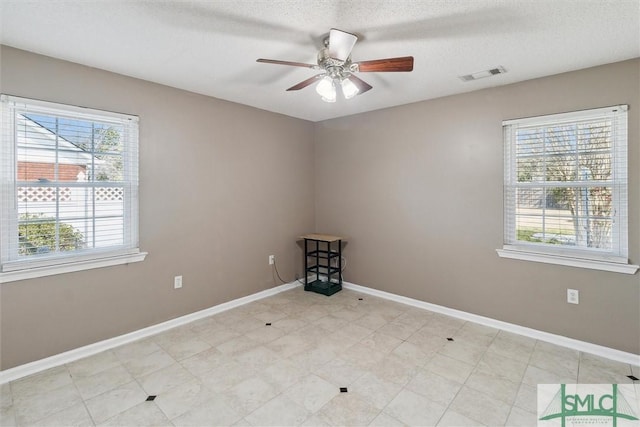 empty room with a textured ceiling, a ceiling fan, visible vents, and baseboards