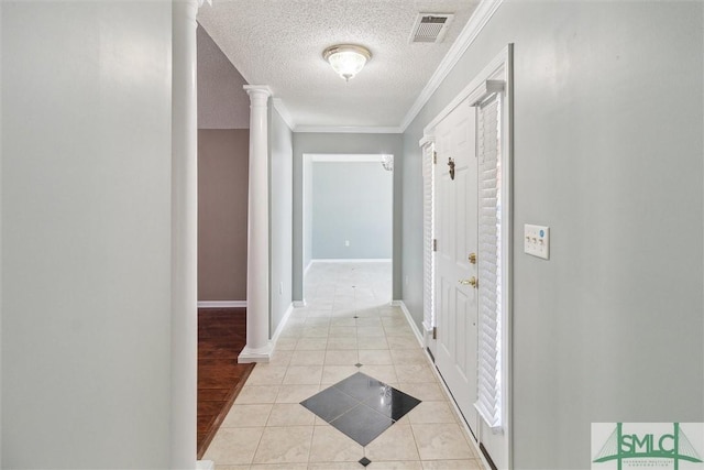 hall featuring visible vents, ornamental molding, a textured ceiling, ornate columns, and light tile patterned flooring