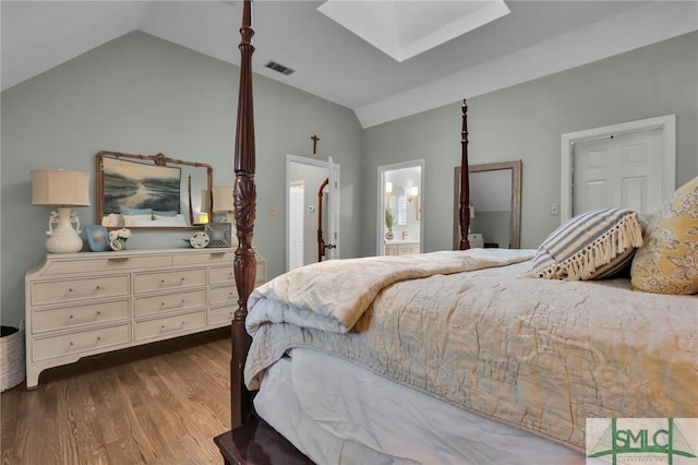 bedroom with ensuite bath, vaulted ceiling with skylight, visible vents, and wood finished floors