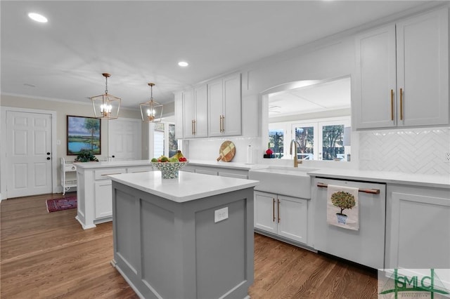 kitchen with light countertops, a kitchen island, a sink, dishwasher, and a peninsula