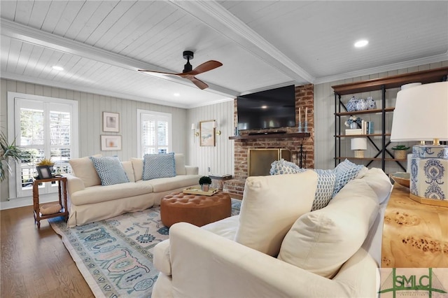 living area featuring crown molding, a fireplace, ceiling fan, wood finished floors, and beamed ceiling