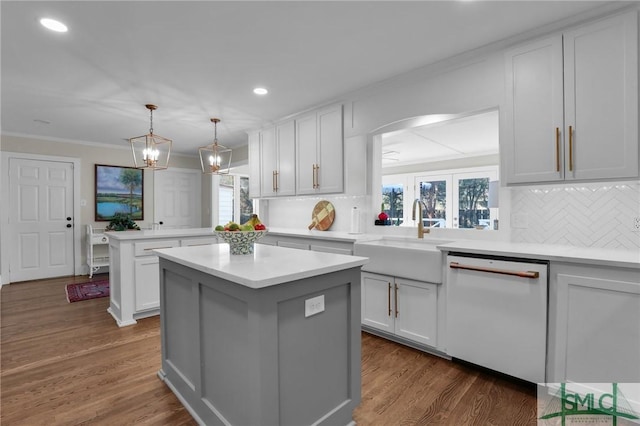 kitchen with white dishwasher, a peninsula, dark wood-style flooring, a sink, and light countertops