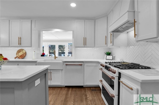 kitchen featuring dark wood-style floors, light countertops, a sink, white appliances, and premium range hood