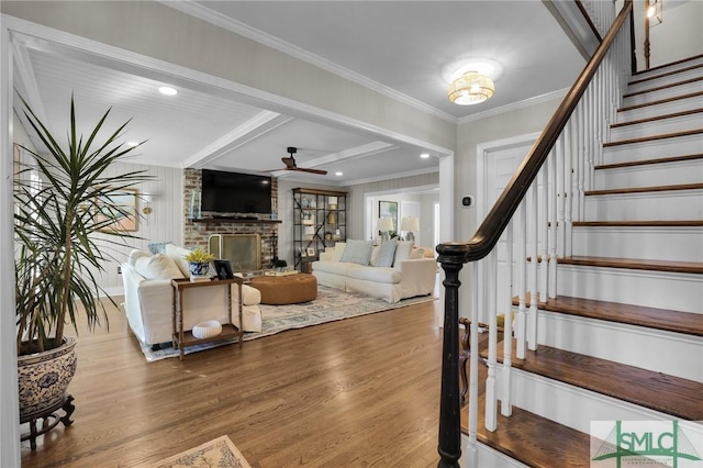 interior space featuring ceiling fan, wood finished floors, stairway, a brick fireplace, and crown molding