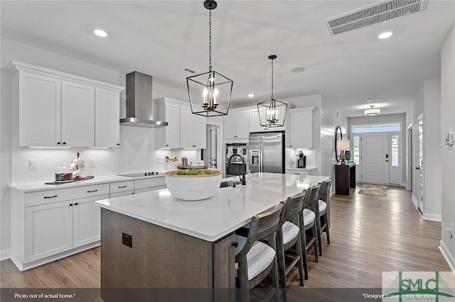 kitchen with black electric cooktop, visible vents, light wood-type flooring, stainless steel refrigerator with ice dispenser, and wall chimney exhaust hood