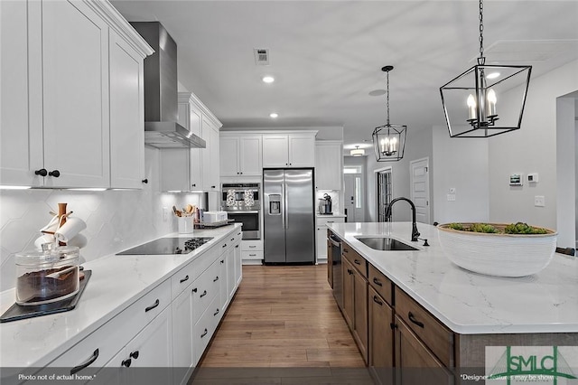 kitchen with visible vents, wood finished floors, stainless steel appliances, wall chimney range hood, and a sink