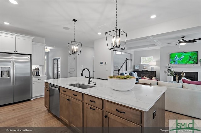 kitchen featuring light wood-style flooring, appliances with stainless steel finishes, open floor plan, and a sink