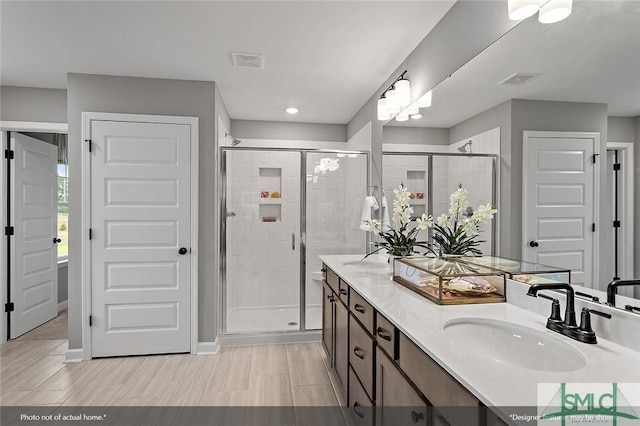 bathroom featuring visible vents, a sink, a shower stall, and double vanity