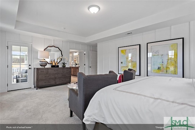 bedroom featuring a tray ceiling, light colored carpet, a decorative wall, visible vents, and ensuite bathroom