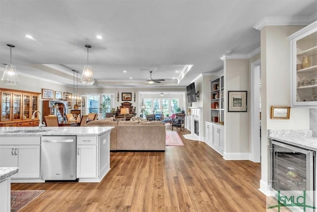 kitchen featuring a sink, light wood-style flooring, a tray ceiling, and stainless steel dishwasher