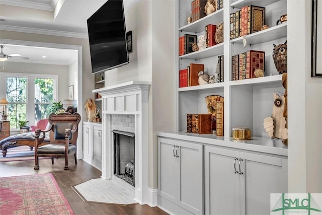 sitting room featuring ceiling fan, dark wood-style flooring, a fireplace, built in features, and ornamental molding