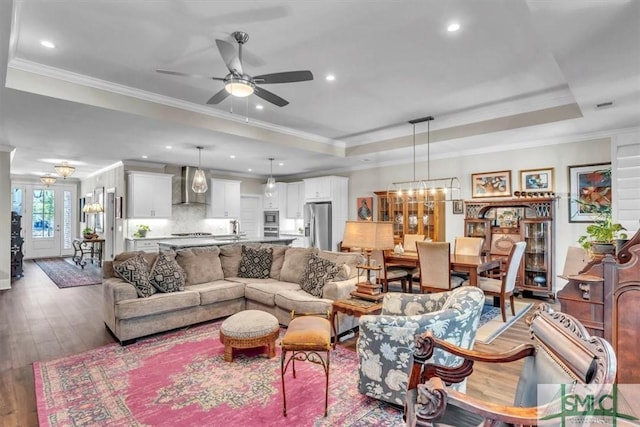 living area with hardwood / wood-style flooring, recessed lighting, ceiling fan with notable chandelier, ornamental molding, and a tray ceiling