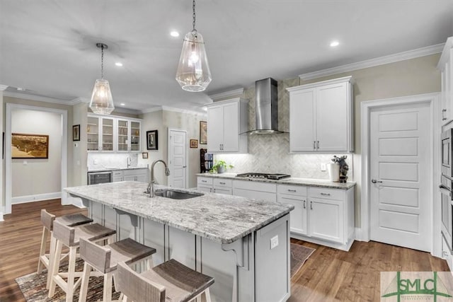 kitchen featuring a kitchen breakfast bar, a sink, wall chimney range hood, and a center island with sink