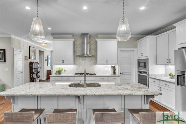 kitchen featuring appliances with stainless steel finishes, white cabinetry, a sink, and wall chimney range hood