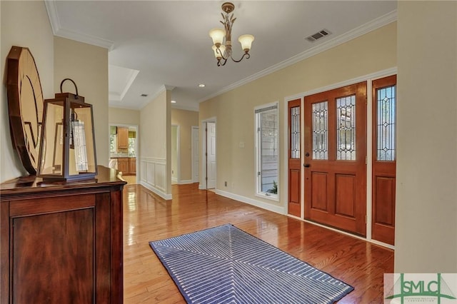 foyer entrance with a notable chandelier, visible vents, baseboards, light wood-type flooring, and crown molding