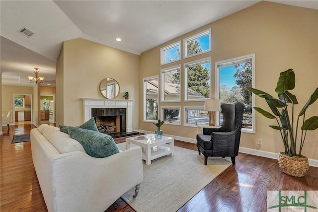 living area featuring a fireplace, visible vents, wood finished floors, a chandelier, and baseboards